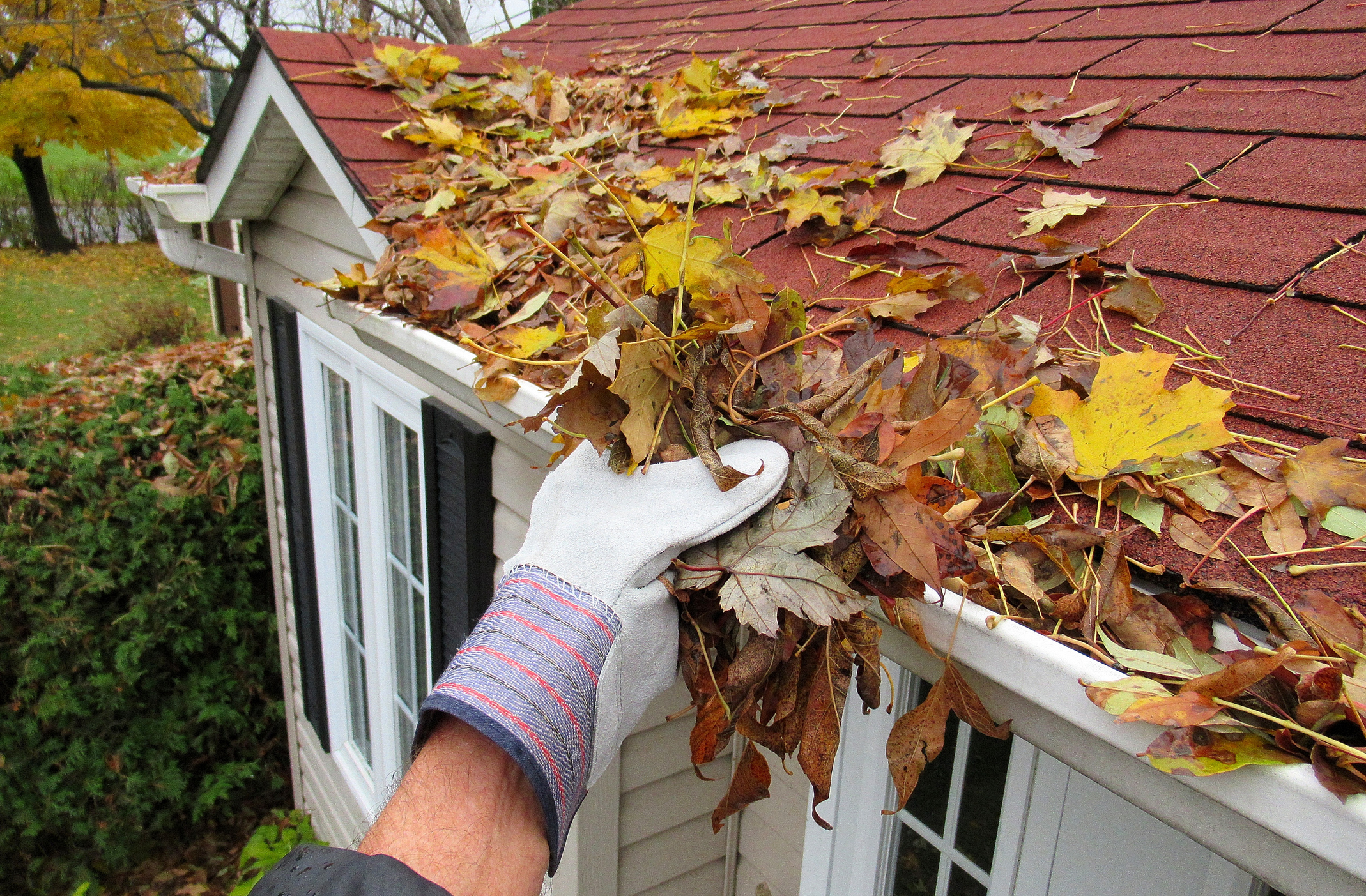 Worker performing gutter cleaning on a Bergen County - NJ roofline while clearing clogged downspout debris